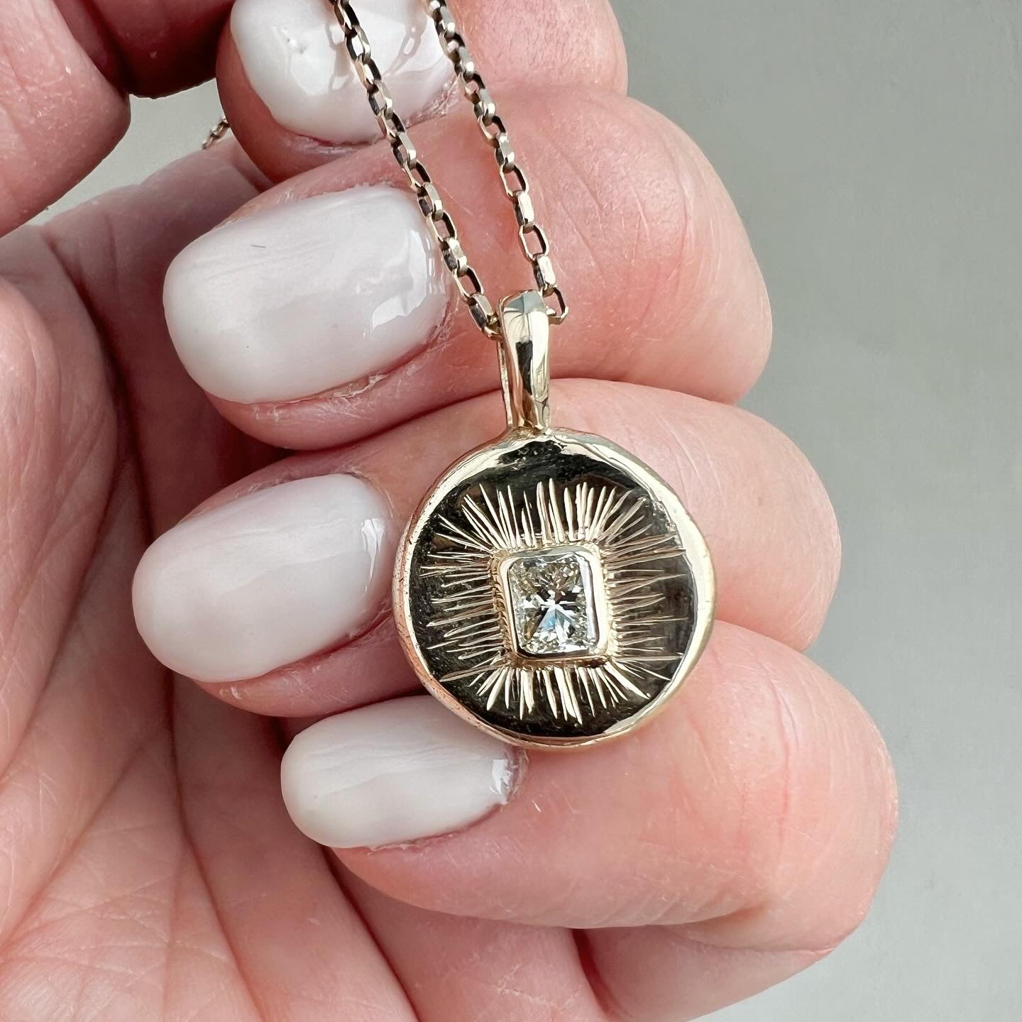 Gold pendant with a diamond held between fingers against a neutral background