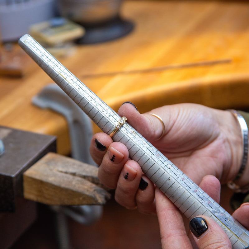 Hand holding a metal ruler with a blurred background of a workshop.