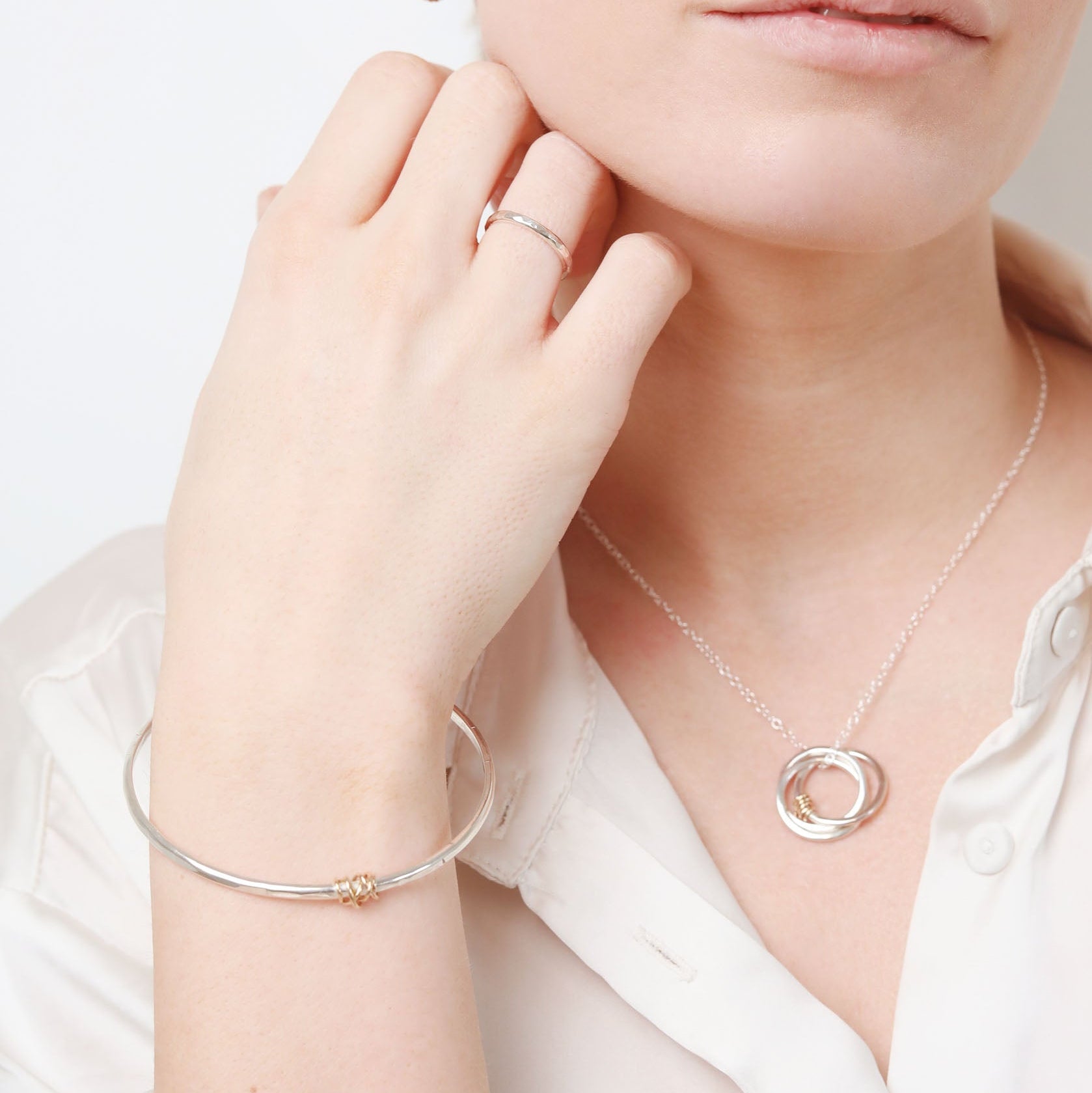 Woman wearing silver jewelry including a necklace, bracelet, and ring on a white background