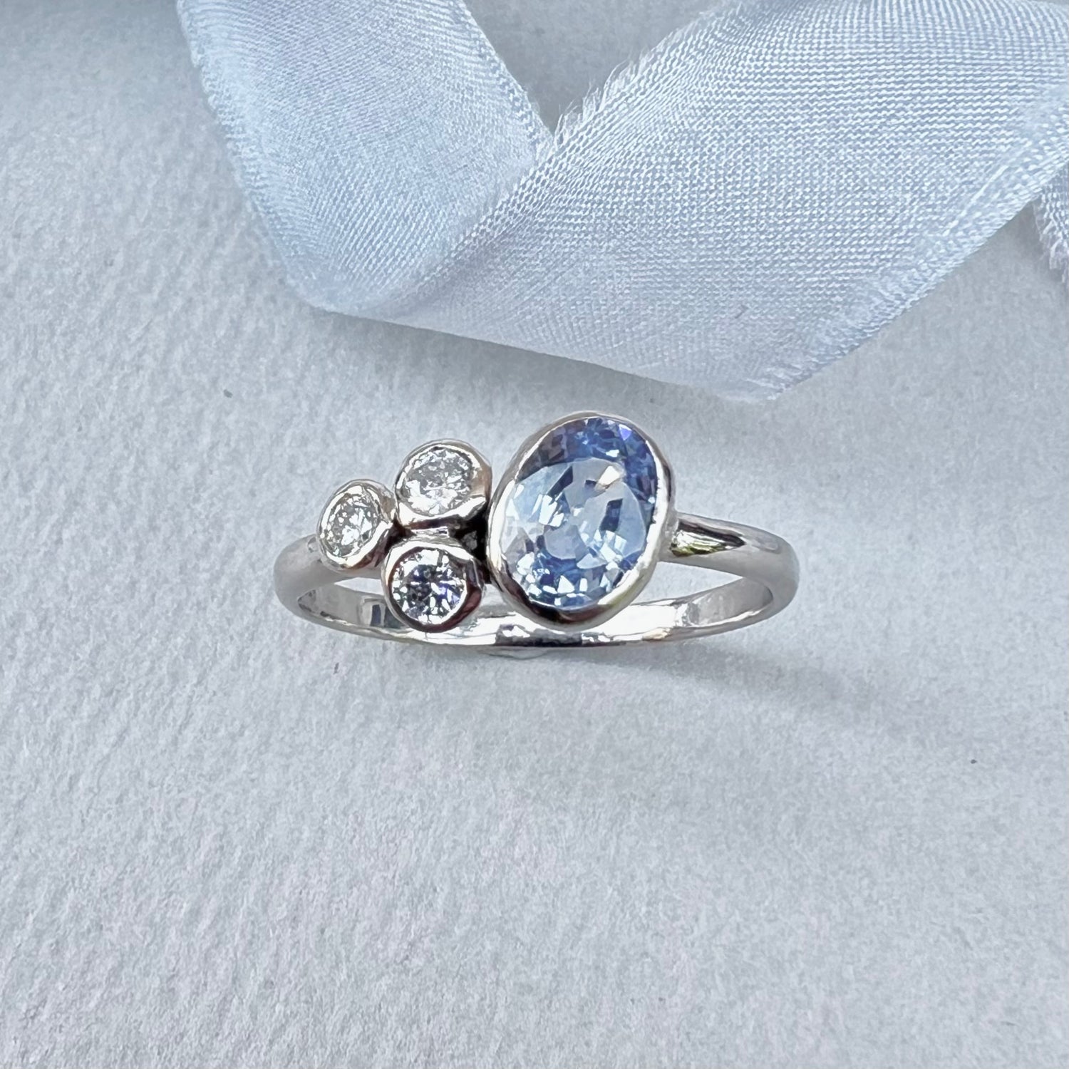 Silver ring with a blue gemstone and smaller diamonds on a light gray background